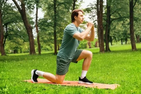 A man performs lunges on a mat during an outdoor workout in a green park. T.. Stock-Fotos