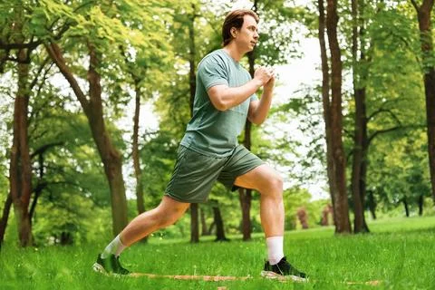 A man performs lunges on an orange mat in a green park. This outdoor fitnes.. Stock-Fotos
