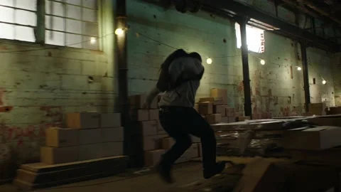 Man performs parkour over crates and boxes in a dark warehouse, in moody lightin Stock Footage 199460174