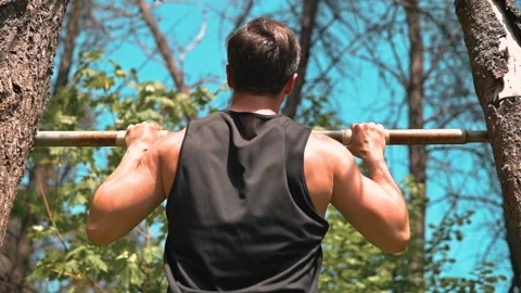 A man performs pull-ups on a horizontal bar positioned between two trees. He Vidéo 339016504