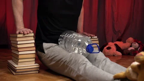 Man performs push-ups using two stacks of books and and bottle of water. Stock Footage 131584109