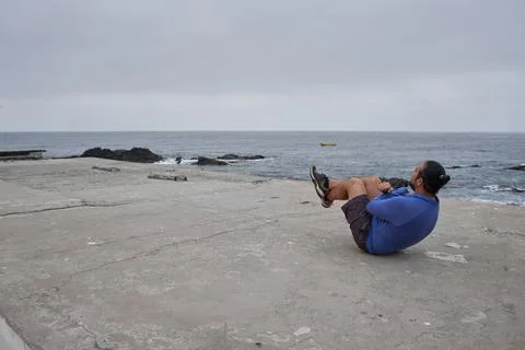 Man performs sit-ups in front of the sea. New normality. Sports Stock Photos