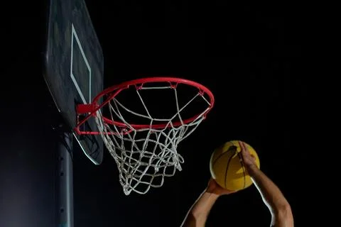 A man performs a slam dunk on a basketball court at night under the glare o.. Фото