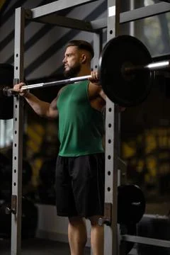 Man performs squats with a barbell in a gym during daytime Stock Photos