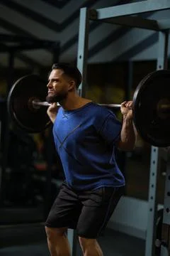 Man performs squats with a barbell in a gym during a workout session focused on Stock Photos