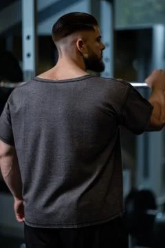 Man performs squats with barbell in gym during evening workout session focused Stock Photos