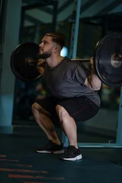 Man performs squats with a barbell in a gym setting during workout session in Stock Photos