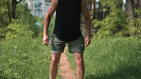 A man performs squats in a green park on a sunny day. He engages in physical Vídeo Stock 339016401