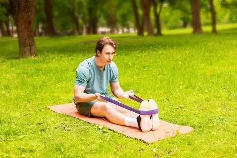 A man performs a stretching exercise with a resistance band on a fitness ma.. Stock Photos