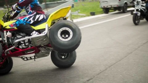A man performs a stunt and rides an ATV on two wheels on the road. Stock Footage 130369921