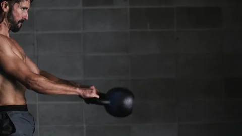 Man performs weight ball swings through legs while bending knees indoors Stock Footage 312766682