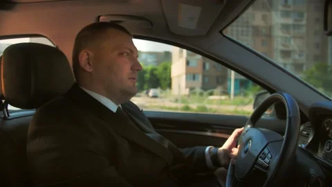 Man personal driver in a suit drives a car through a sunny city. Stock Footage 201086389