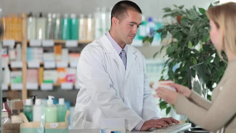 Man pharmacist is working at computer, collaborate with girl client.Electronic Stock Footage 313874413