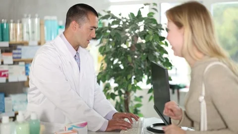 Man pharmacist is working at computer, communicate with girl customer Stock Footage 335614111
