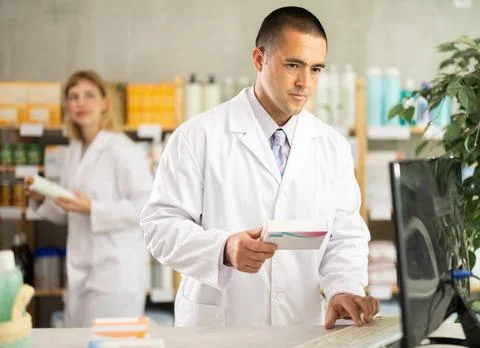 Man pharmacy employee works with computer, girl assistant work in background Stockfoto's