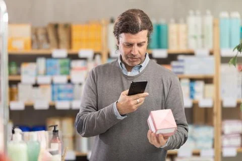 Man in pharmacy scans QR code on emollient cream product 스톡 사진