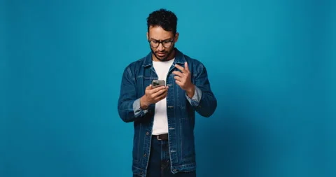 Man, phone and doubt in studio with scam, phishing and reading post on blue Stock Footage 314371455