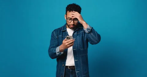 Man, phone and shocked in studio with scam, phishing and reading post on blue Stock Footage 314371504