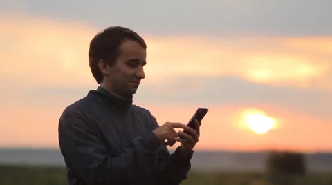 The man on the phone compose sms. Beautiful sunset on the background Stock Footage 64600776