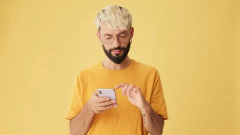 Man with phone in his hands scrolls, chooses, makes purchases isolated on yellow Stock Footage 255964548