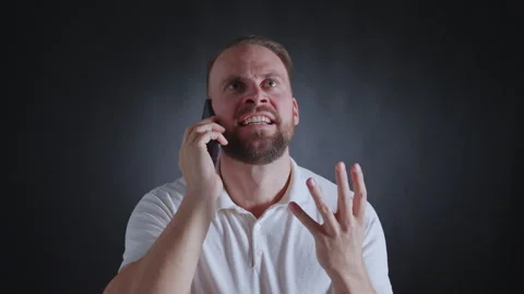 Man on phone, looking concerned, white shirt, dark background. Vidéo 308073174