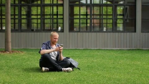 Man with phone sits on the grass 스톡 동영상 91231565