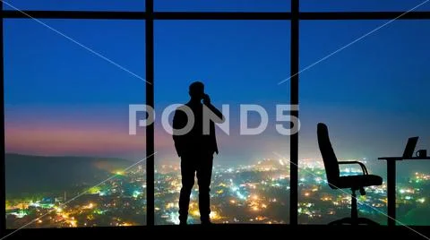 The man phones near the panoramic window on a night city background Stock Photos