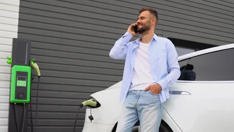 A man phoning while charging car at electric vehicle charging station Stock Footage 251764697