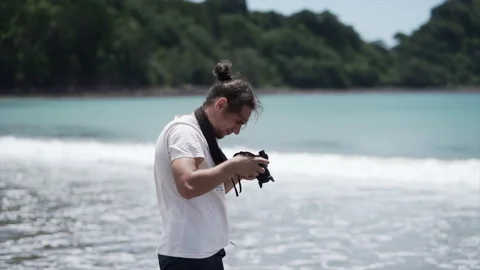 Man photographer looking at camera on the beach new chums beach, new zealand Stock Footage 221230539