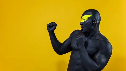 Man pick on copy space. Bodybuilder athlete with yellow face art and black body Stock Footage 128883907