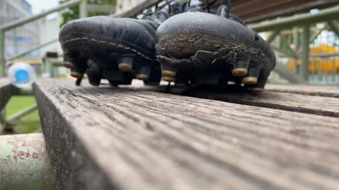 Man pick up worn off soccer cleats from wooden bench. Outdoor football field Stock Footage 287682807
