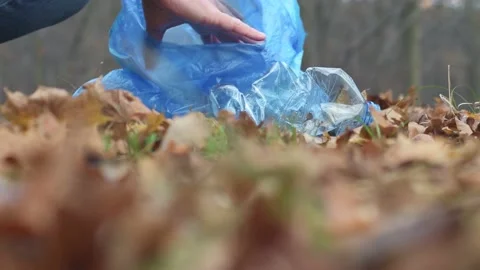 A man picking up a plastic bottle and putting it in a blue garbage bag. Stock Footage 225072159