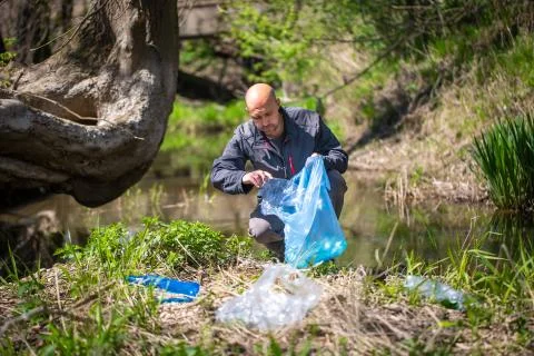 Man picking up plastic bottle, garbage collecting in the forest cleaning planet 写真素材