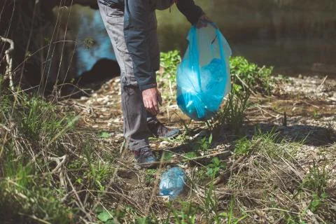 Man picking up plastic bottle, garbage collecting in the forest cleaning planet 库存照片