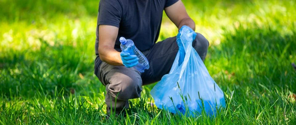 Man picking up plastic bottle, garbage collecting in a forest cleaning planet 库存照片