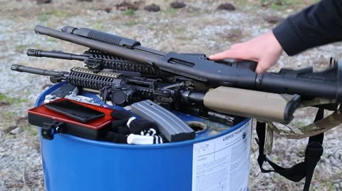 Man picking up a shot gun from a barrel with other rifles and ammunition laying 库存影片 59104971