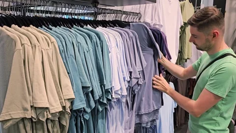 Man picking up t shirt from rack in clothing store. Male customer Stock Footage 313149116