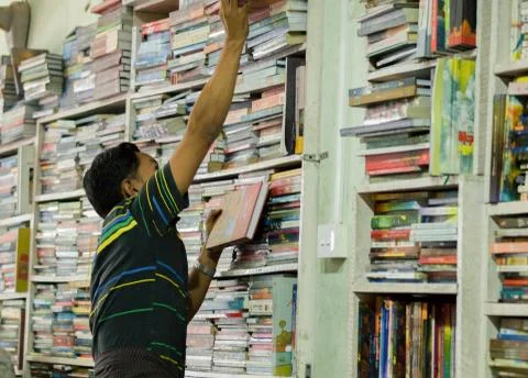MAN PICKS UP A BOOK FROM BOOKSHELF Stock Photos