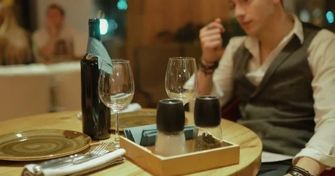 Man picks up a bottle of wine and pours it into glasses. Dinner in a cozy cafe Stock Footage 119452298