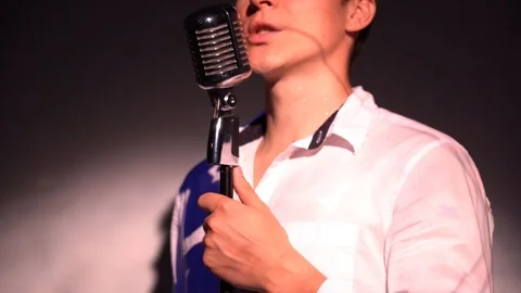 Man picks up chrome mic on scene in dark club and says 1, 2, 3. Spotlights shine Stock Footage 118529211