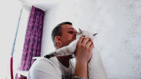 The man picks up his cat and hugs it to him. He loves his animal very much. Stock Footage 320556632