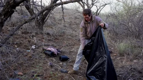 A man picks up litter left by illegal immigrants in the Arizona desert Stock Footage 263144043