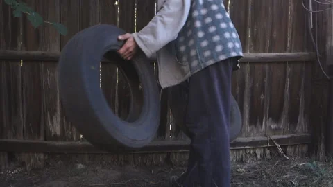 A man picks up old wheels thrown into a fence. Stock Footage 211296101