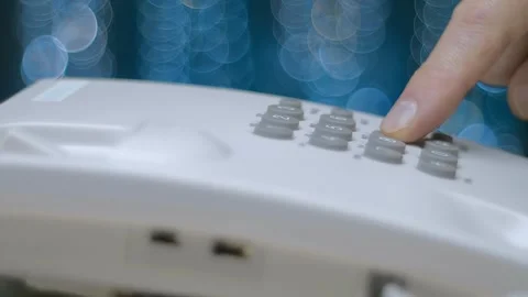 A man picks up the phone, dials 911 on a push-button wired white telephone Stock Footage 259680131