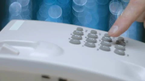 A man picks up the phone, dials a number on a push-button wired white telephone Stock Footage 259679986
