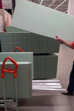 Man picks up plasterboard panel at hardware store. Stack of panels demonstr.. Stock Photos