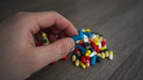 A man picks up a red and blue pill from a handful of pills Stock Footage 212964317