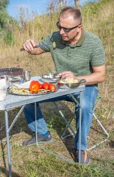 A man on a picnic on a summer day eats baked vegetables Stock Photos
