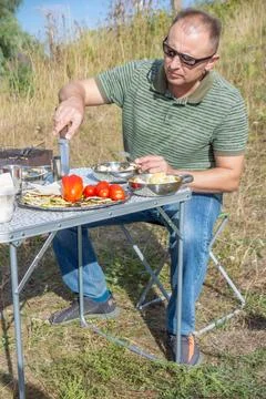 A man on a picnic on a summer day eats baked vegetables. Stock Photos