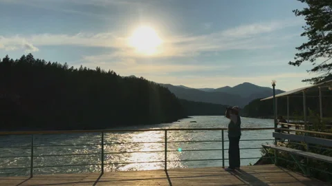 A man on a pier looking in a binocular at a mountain scenery Stock Footage 92847853